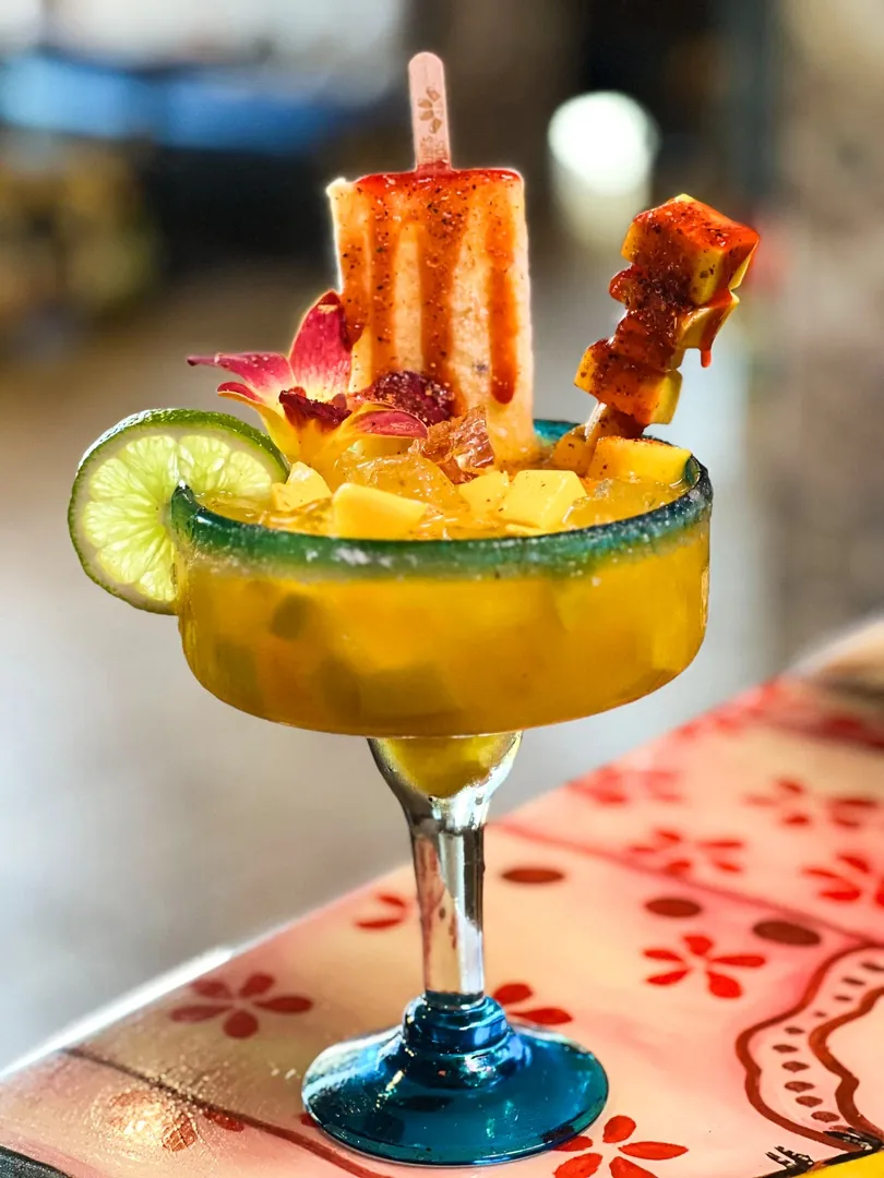 A mango margarita topped with a chili-dipped popsicle